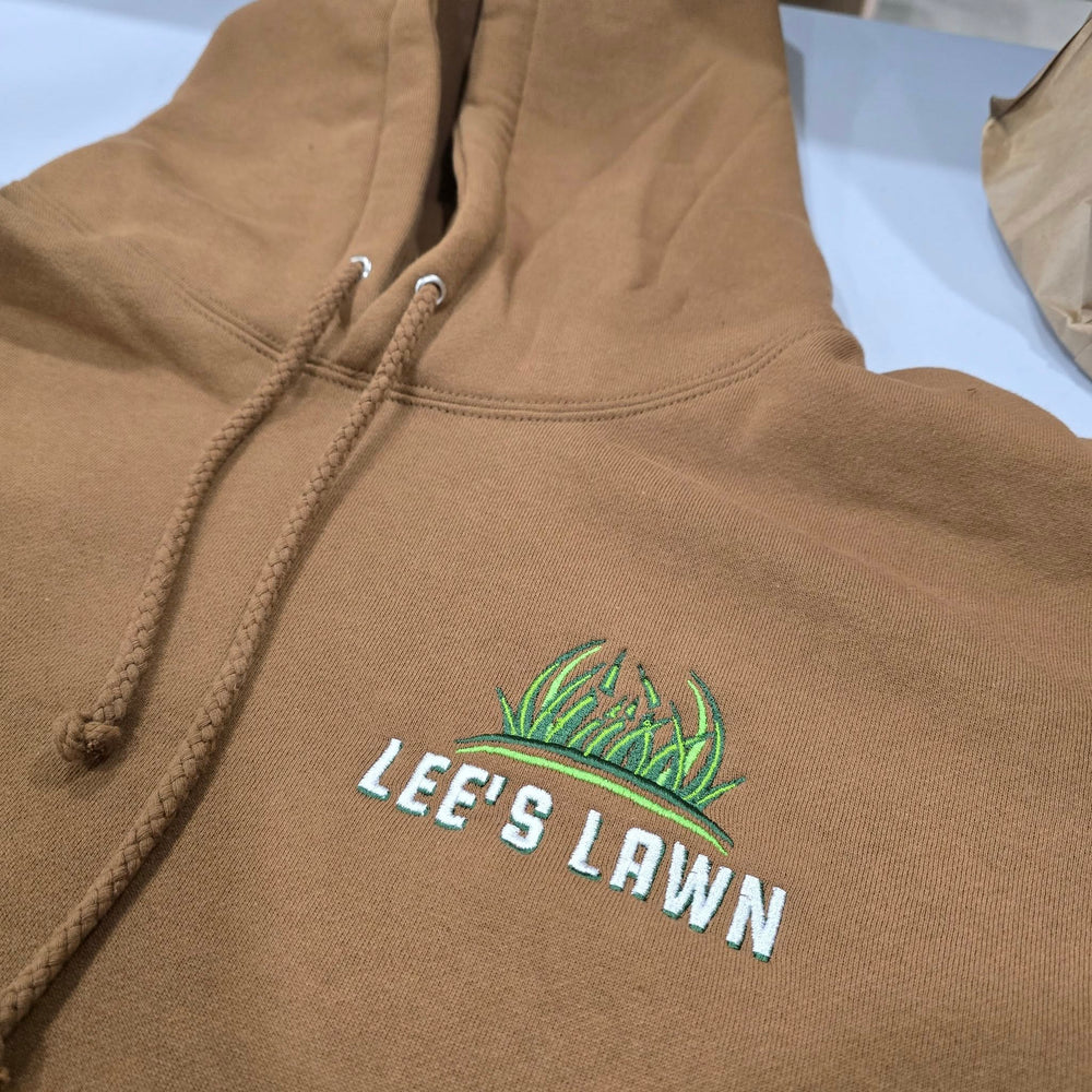 Brown hoodie with 'LEE'S LAWN' logo on a light blue surface