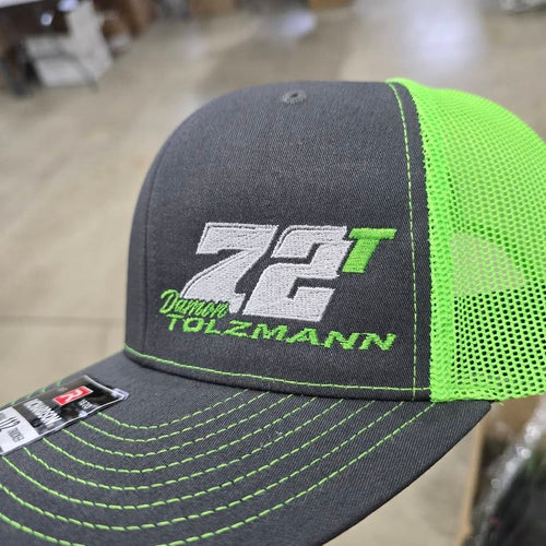 Gray and green cap with '72T Damon Tolzmann logo on a blurred background