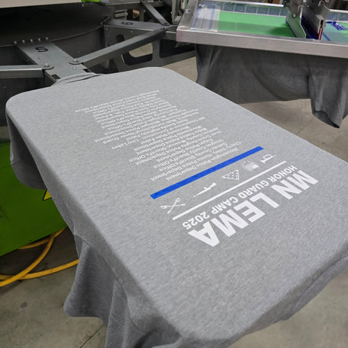 Gray t-shirt with printed text and graphics on a printing machine.